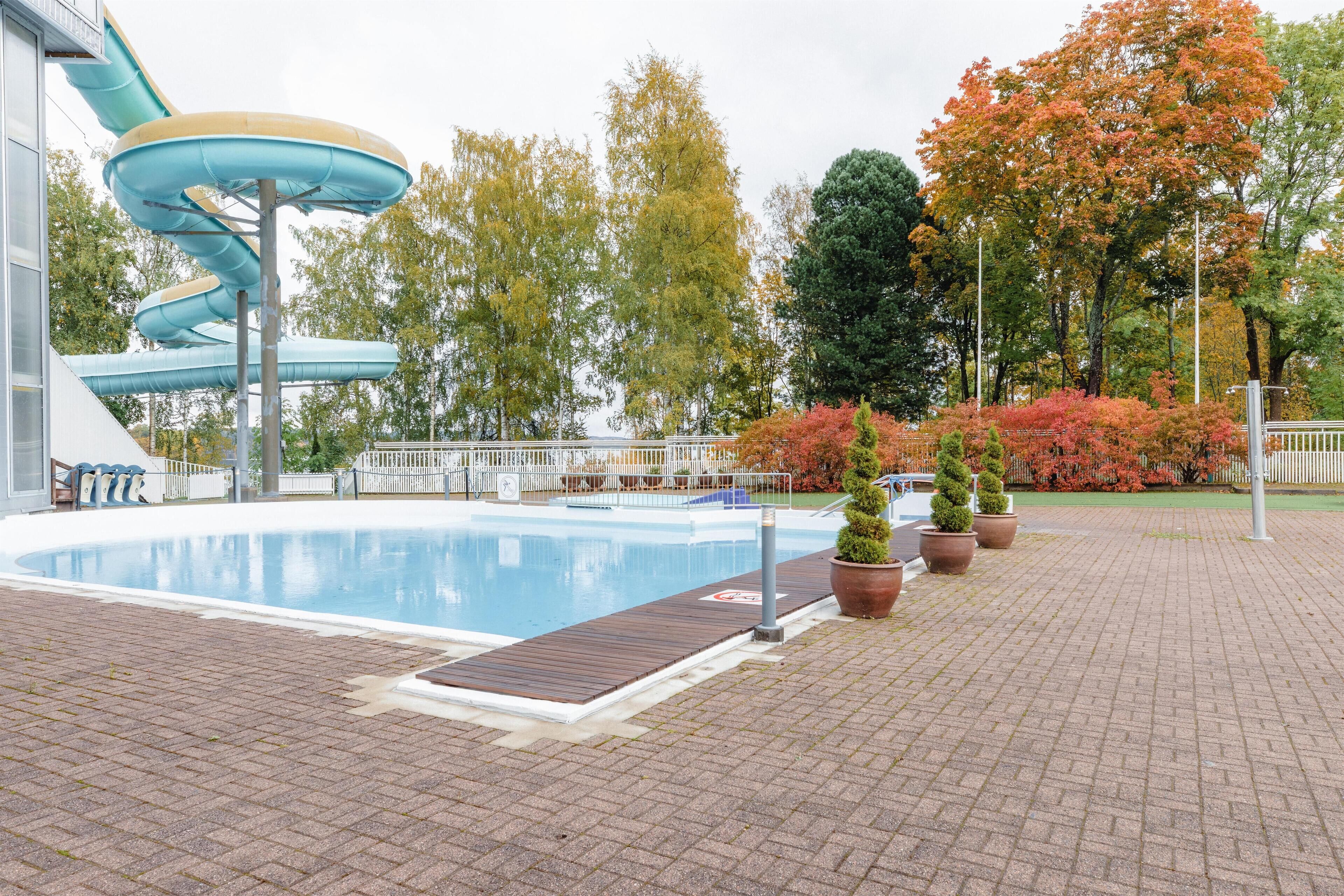 Une piscine avec un toboggan, entourée d’arbres et de plantes en pot.
