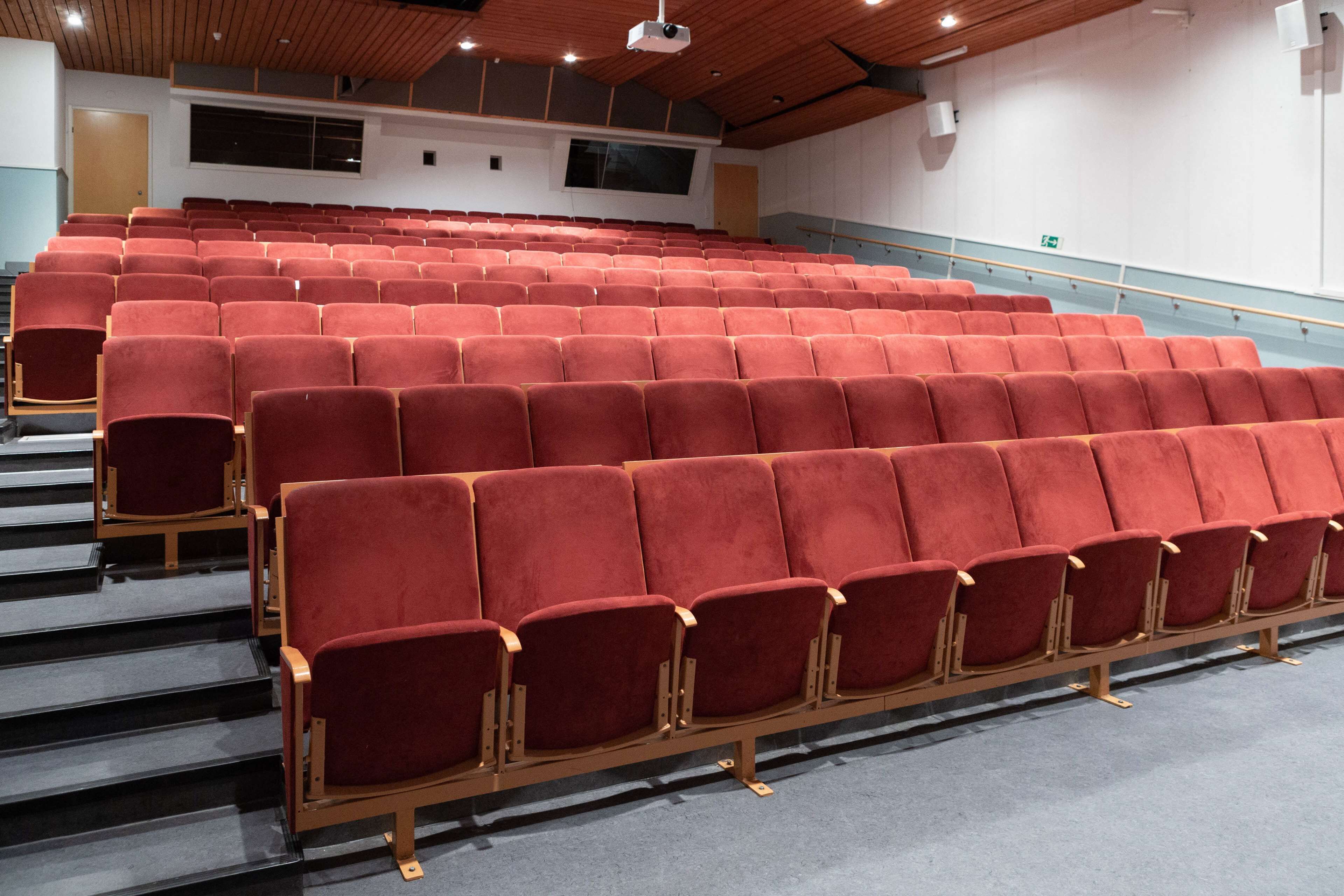 A theater with rows of red seats, wooden stage, and a balcony.