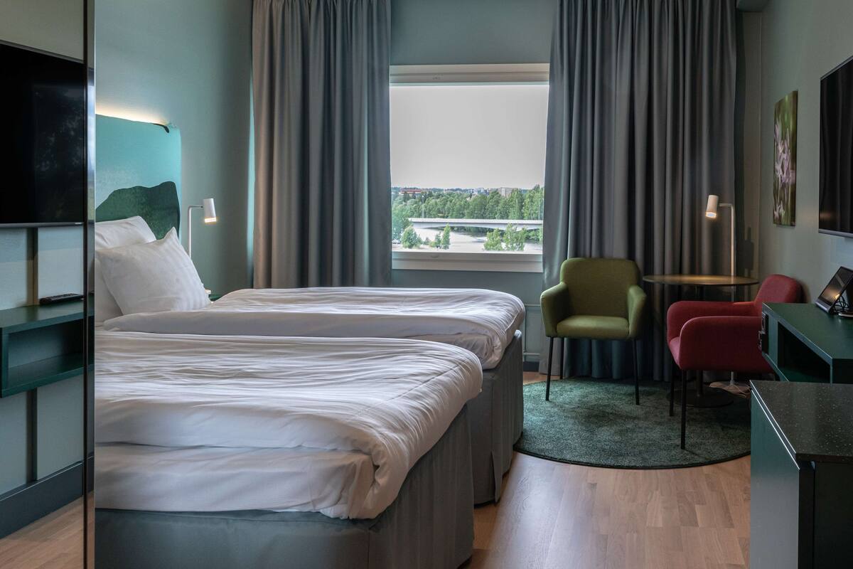 Hotellihuone, jossa on sänky, työpöytä, tuoli ja televisio.