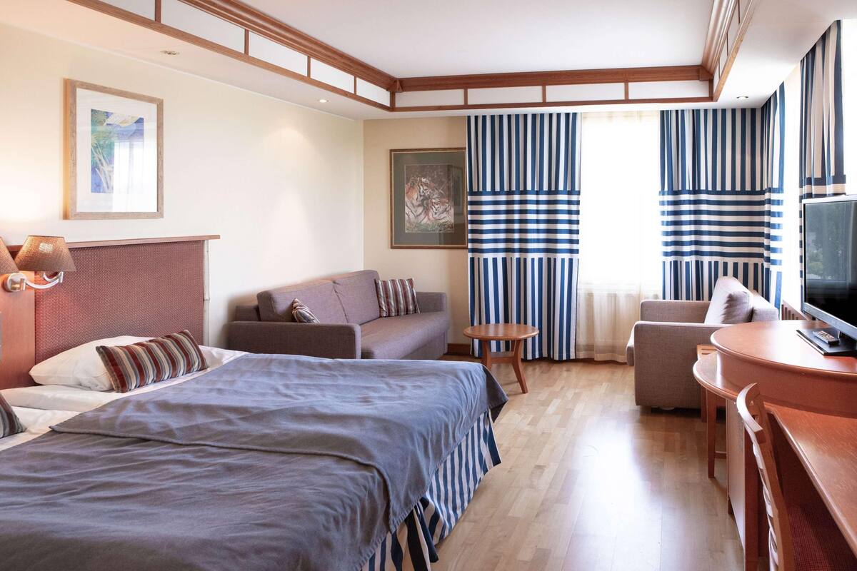 Hotellihuone, jossa on sänky, kaksi sohvaa, televisio ja pieni pöytä.