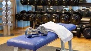 A gym with a blue bench, dumbbells, and a white towel.