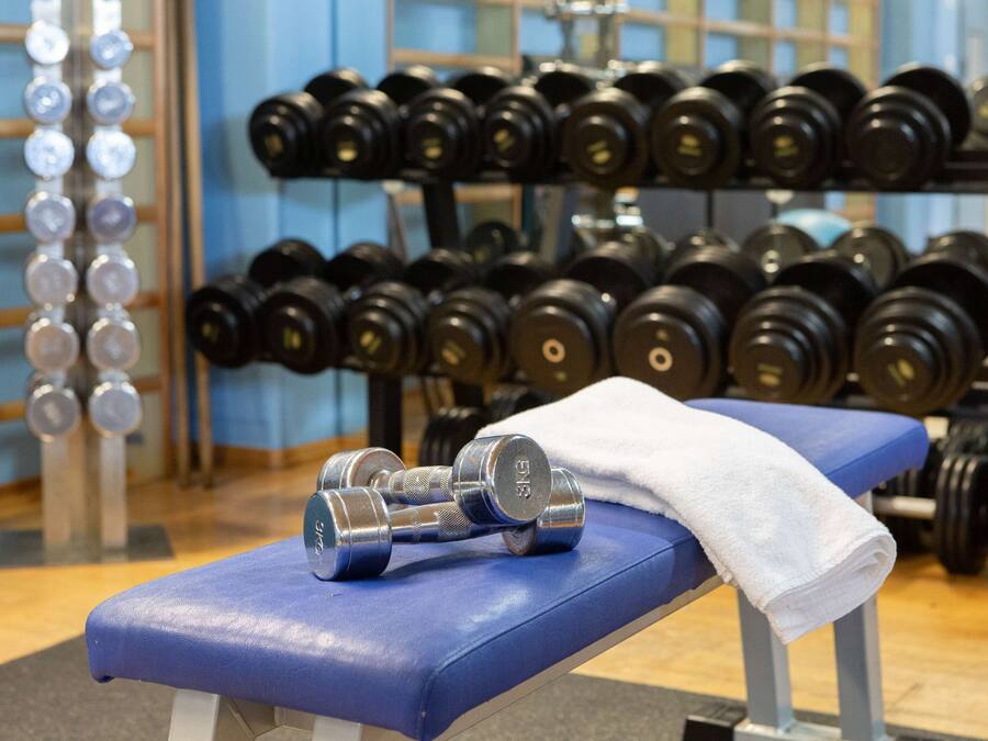 A gym with a blue bench, dumbbells, and a white towel.