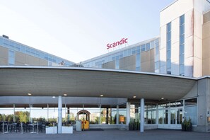 A modern building with a covered entrance, glass windows, and the name "Scandic" prominently displayed.