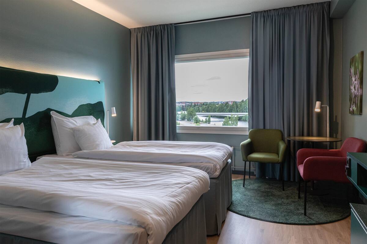 Hotellihuone, jossa on kaksi sänkyä, näköala sillalle sekä työpöytä ja tuoli.