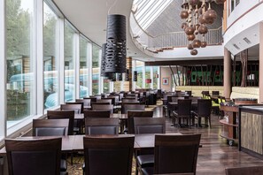 A spacious dining area with high ceilings and large windows, featuring modern furniture and unique hanging light fixtures.