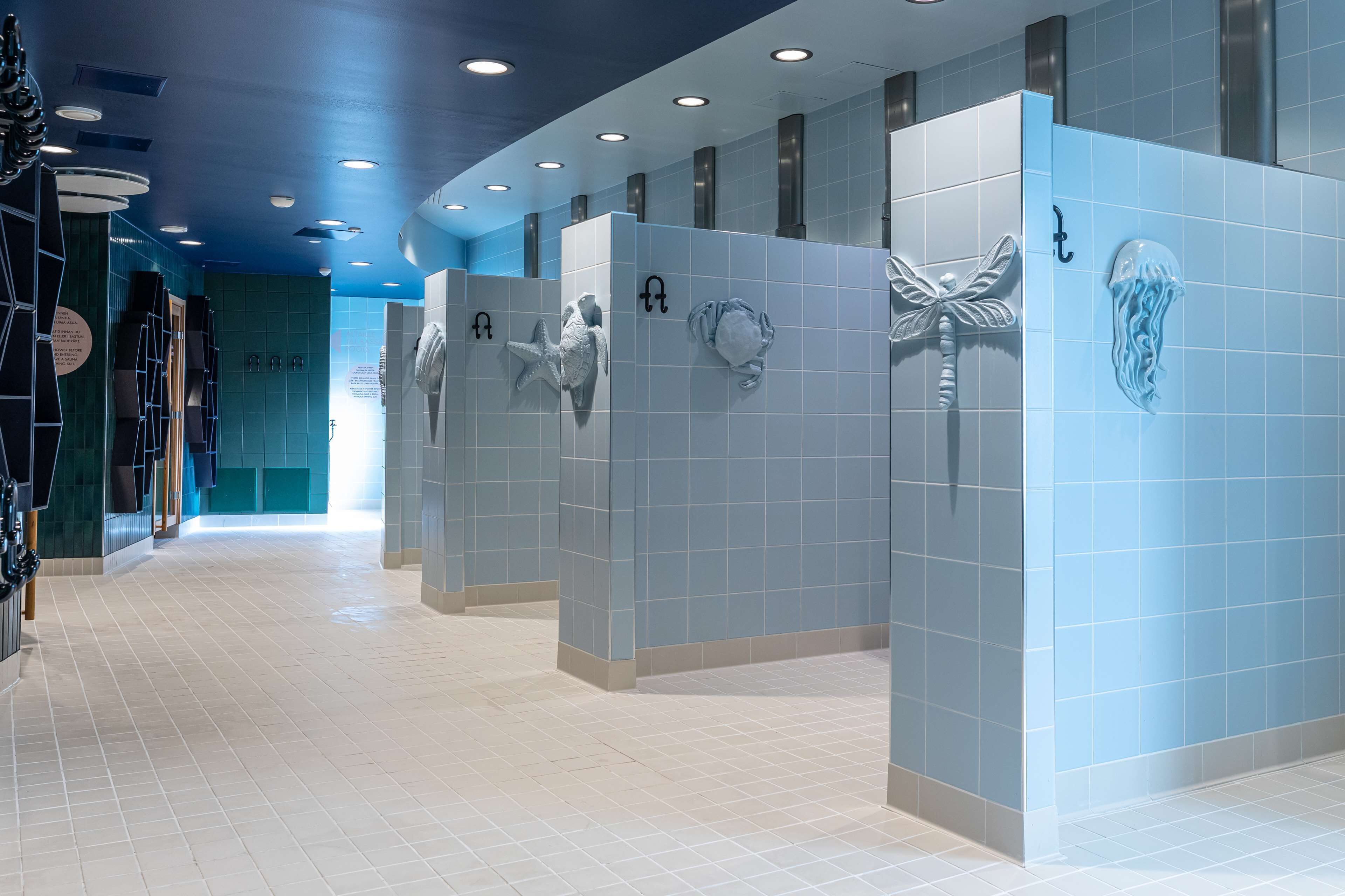 A modern bathroom with blue tiled walls, white floor tiles, and decorative shark and jellyfish wall art.