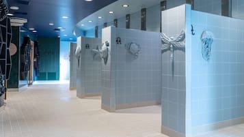 A modern bathroom with blue tiled walls, white floor tiles, and decorative shark and jellyfish wall art.