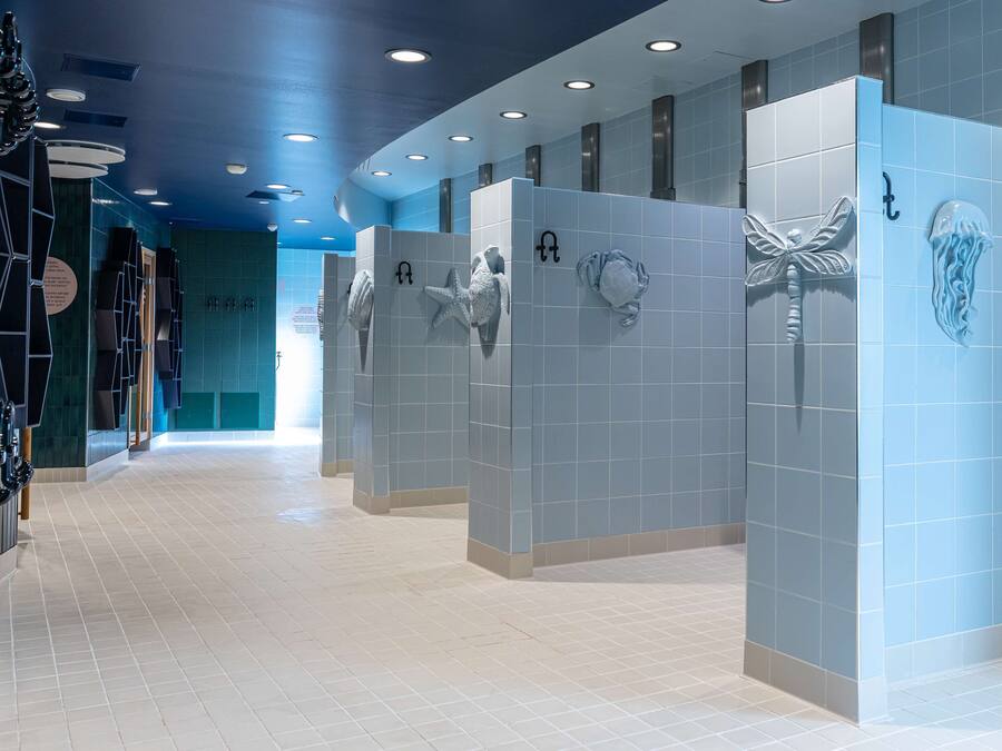 A modern bathroom with blue tiled walls, white floor tiles, and decorative shark and jellyfish wall art.