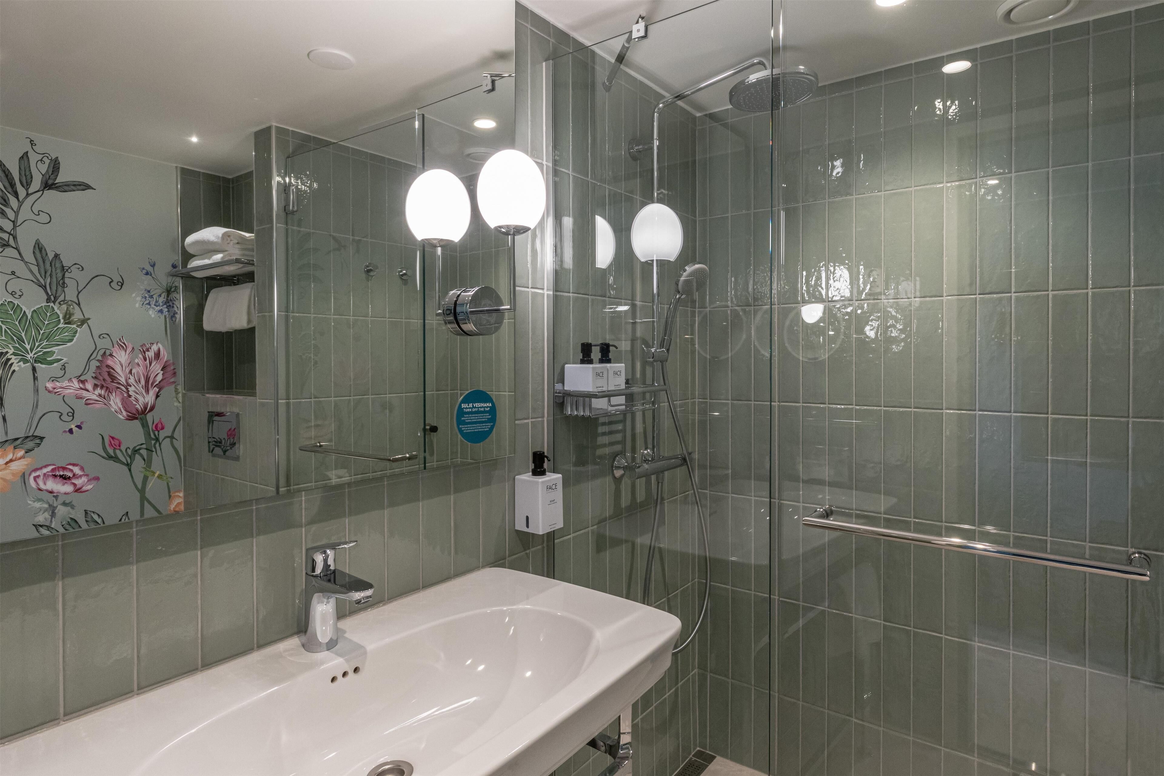 A modern bathroom with a glass shower enclosure, a white sink, and a mirror with floral wallpaper.