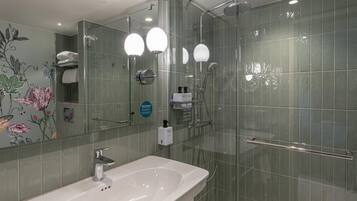 A modern bathroom with a glass shower enclosure, a white sink, and a mirror with floral wallpaper.
