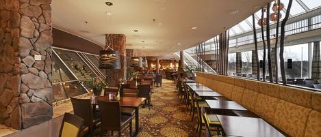 A spacious restaurant with a stone wall, patterned carpet, and a view through large windows.