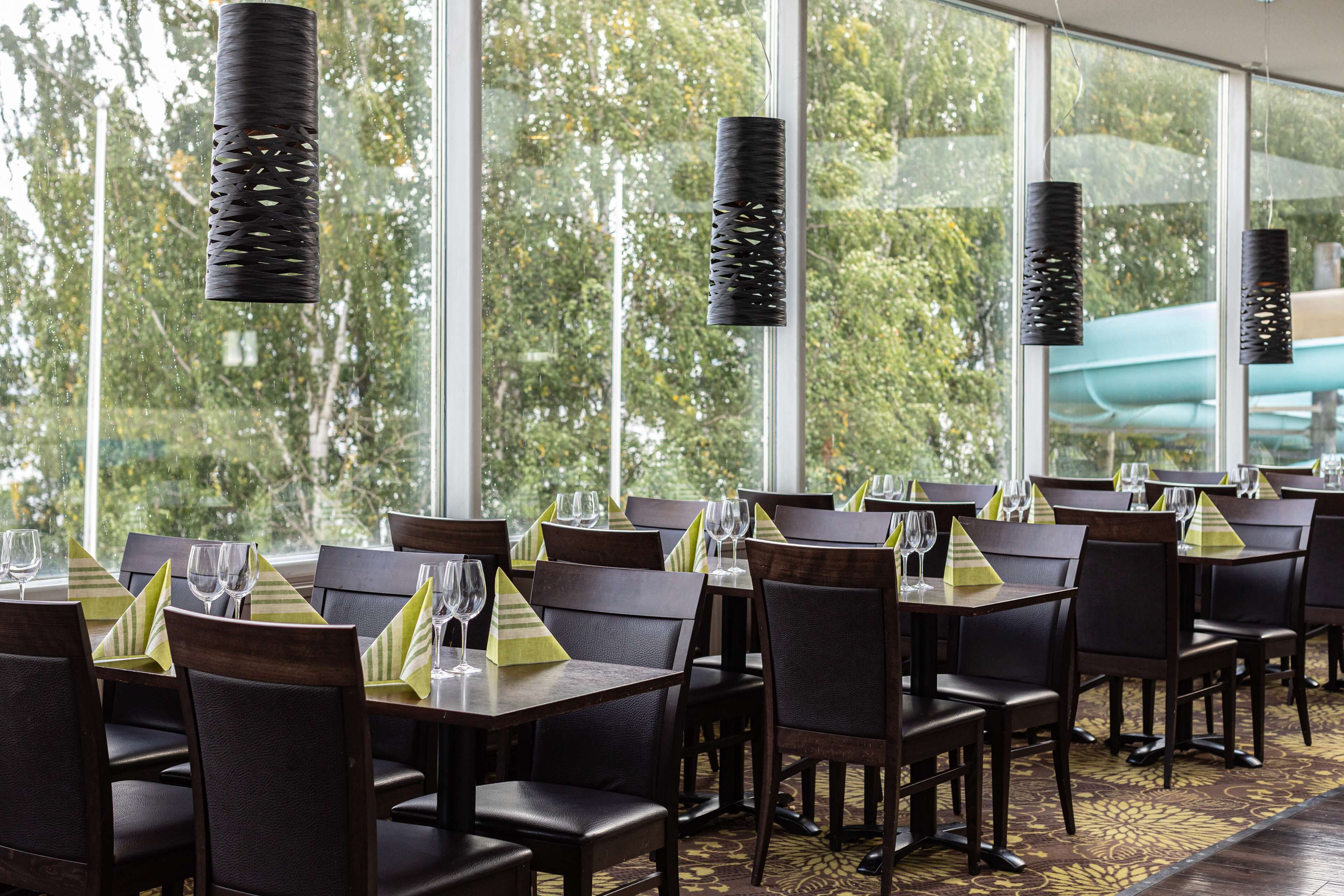 Een restaurant met gedekte tafels, grote ramen en hangende lampen.