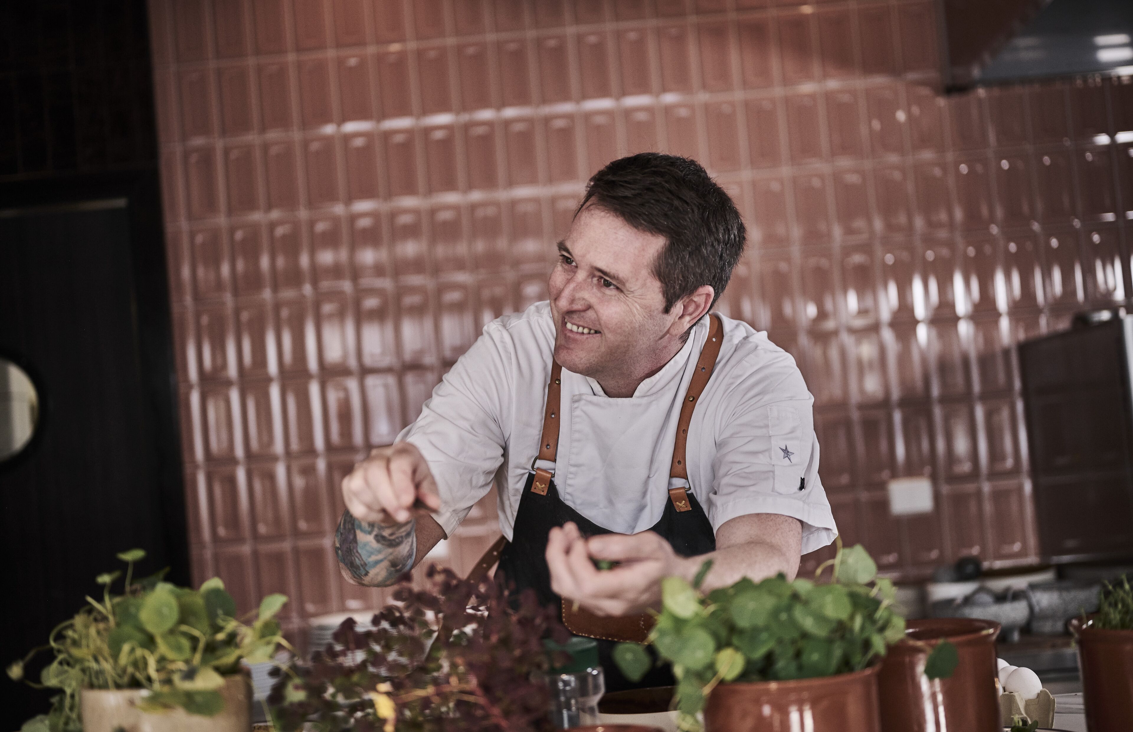 A person in a white shirt and apron working with plants at a table.