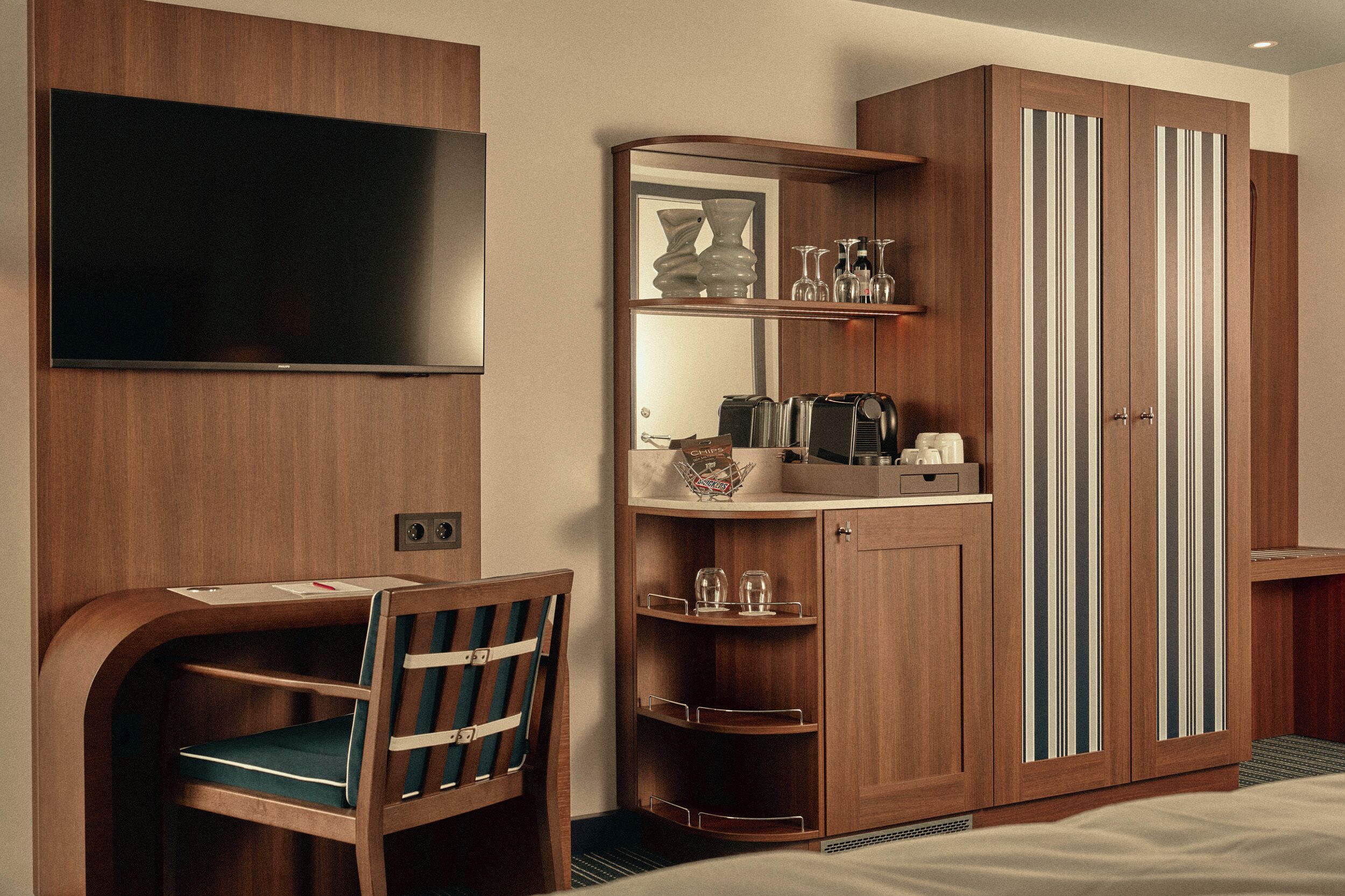 Habitación de hotel con televisor, escritorio con silla, minibar y armario con puertas a rayas.