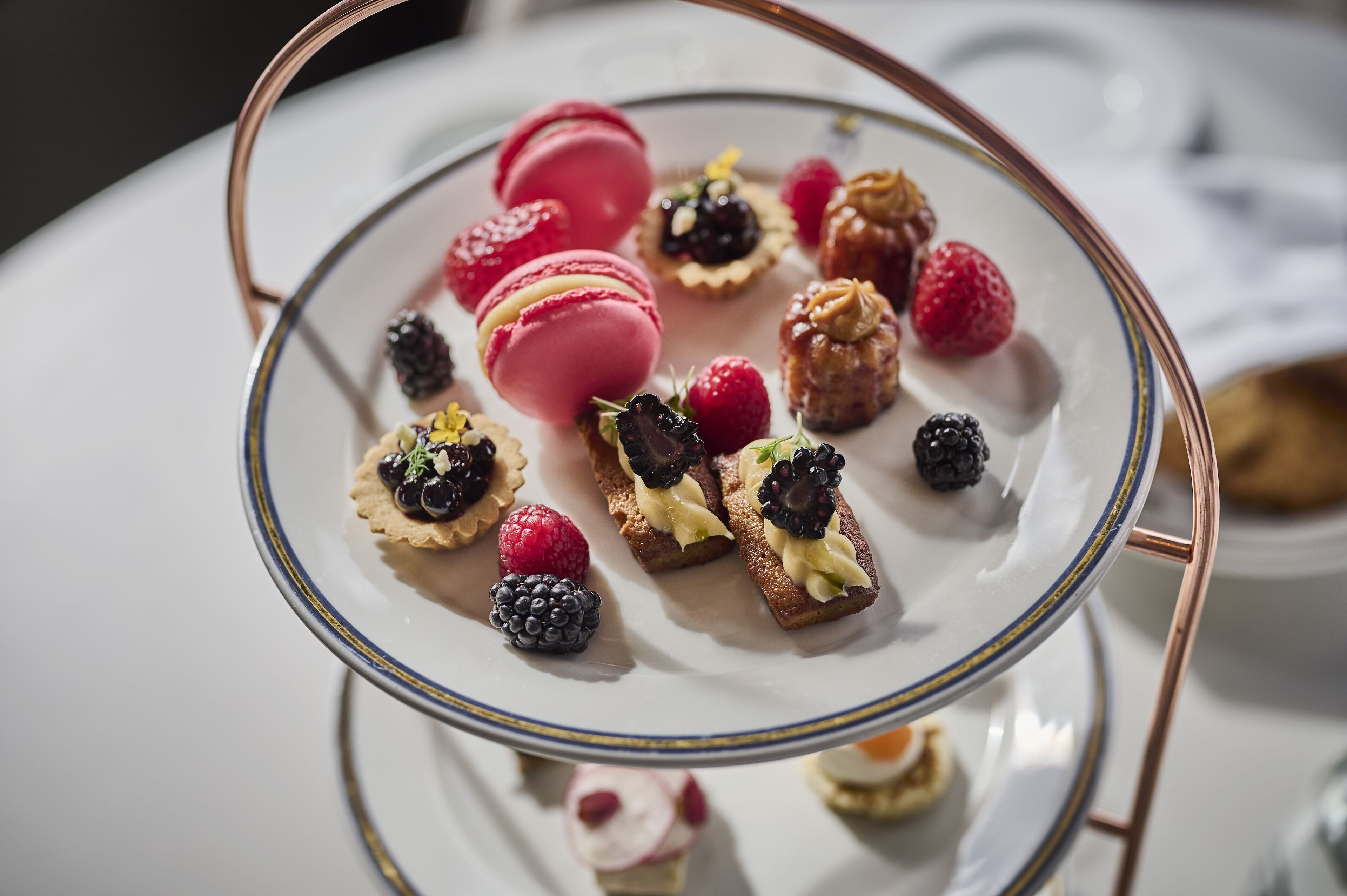 Un piatto dessert a più livelli con macarons, frutti di bosco e piccoli pasticcini.