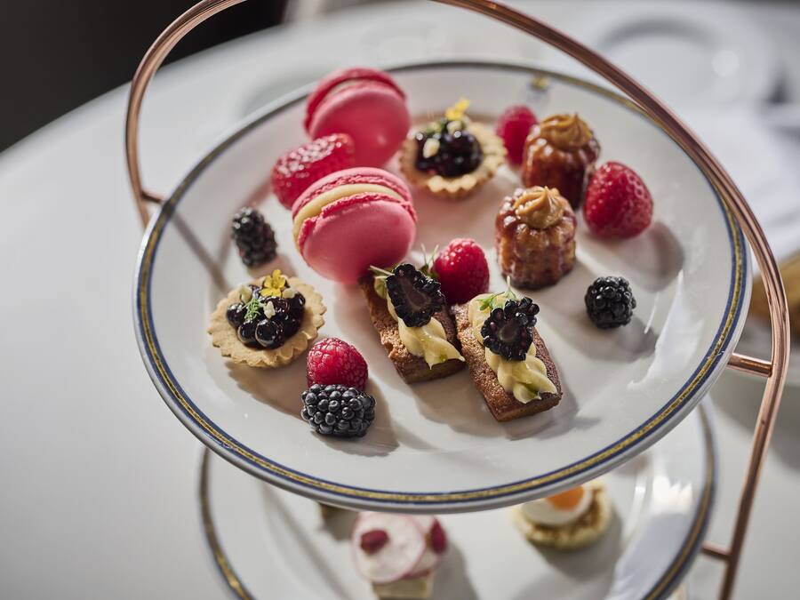Un plato de postres con varios niveles, con macarons, frutos rojos y pequeñas pastas.