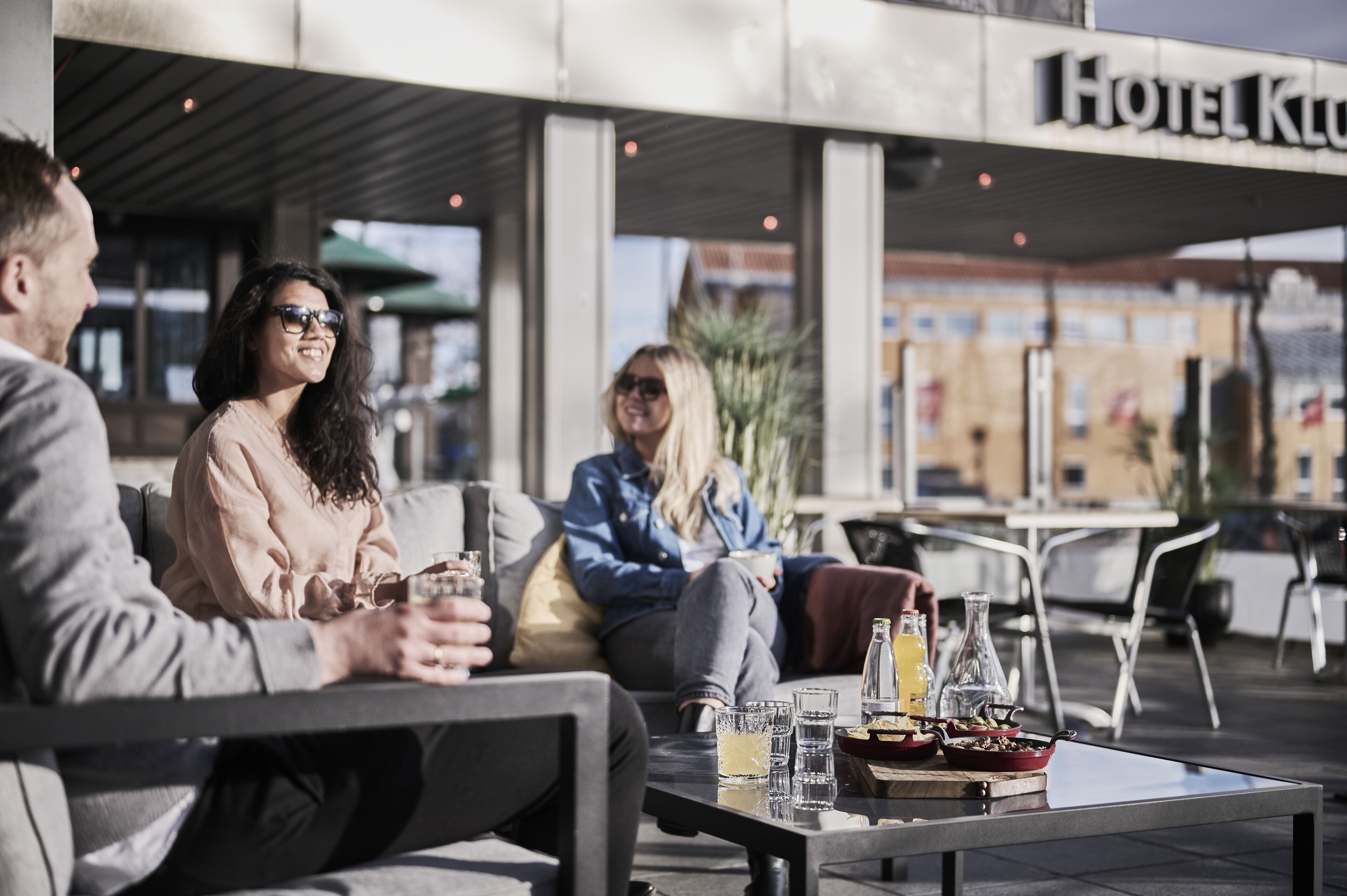 An outdoor seating area with tables and chairs, a menu with food and drinks, and a building with a sign that reads "Hotel Klub".