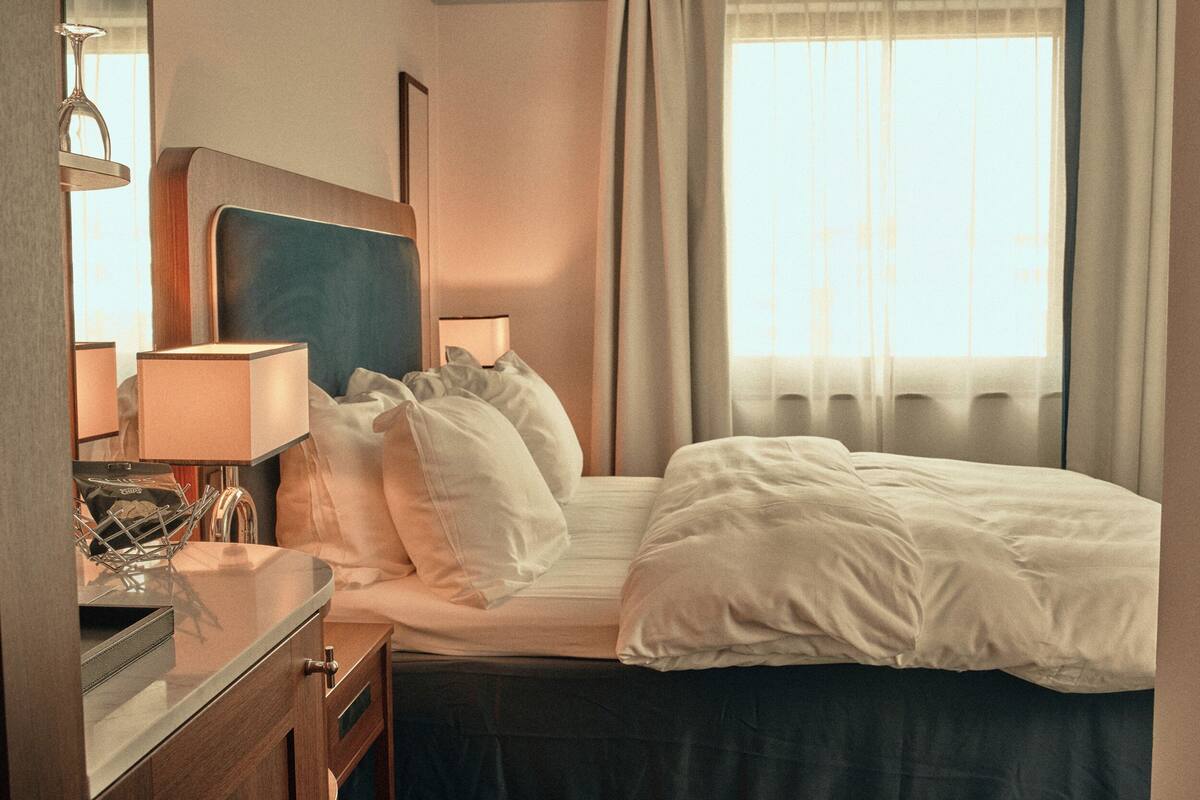 A hotel room with a bed, bedside lamps, a nightstand, and a window with curtains.