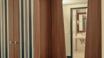 Un armario de madera con rayas verticales y un espejo de marco ondulado que refleja un baño con lavabo y espejo.
