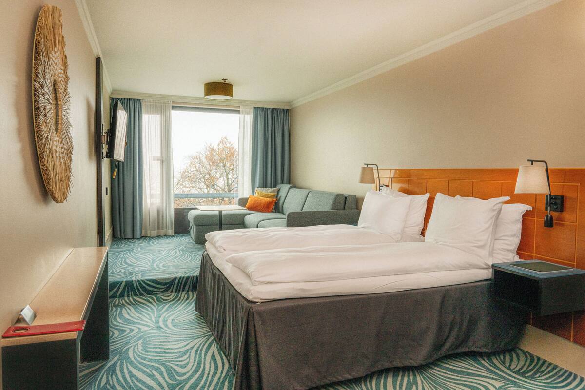 A hotel room with a large bed, a sofa, a desk, and a window with curtains.