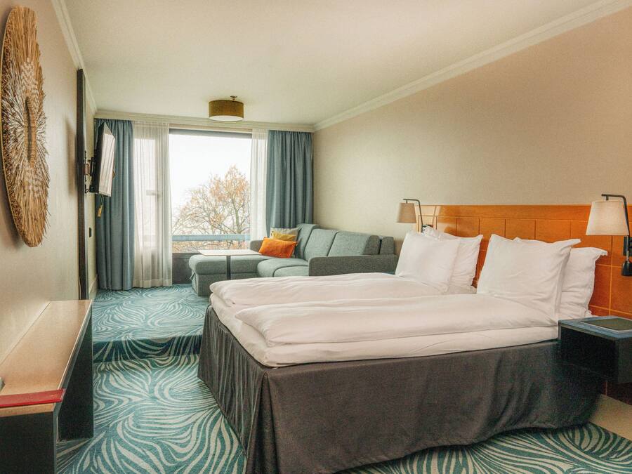 A hotel room with a large bed, a sofa, a desk, and a window with curtains.