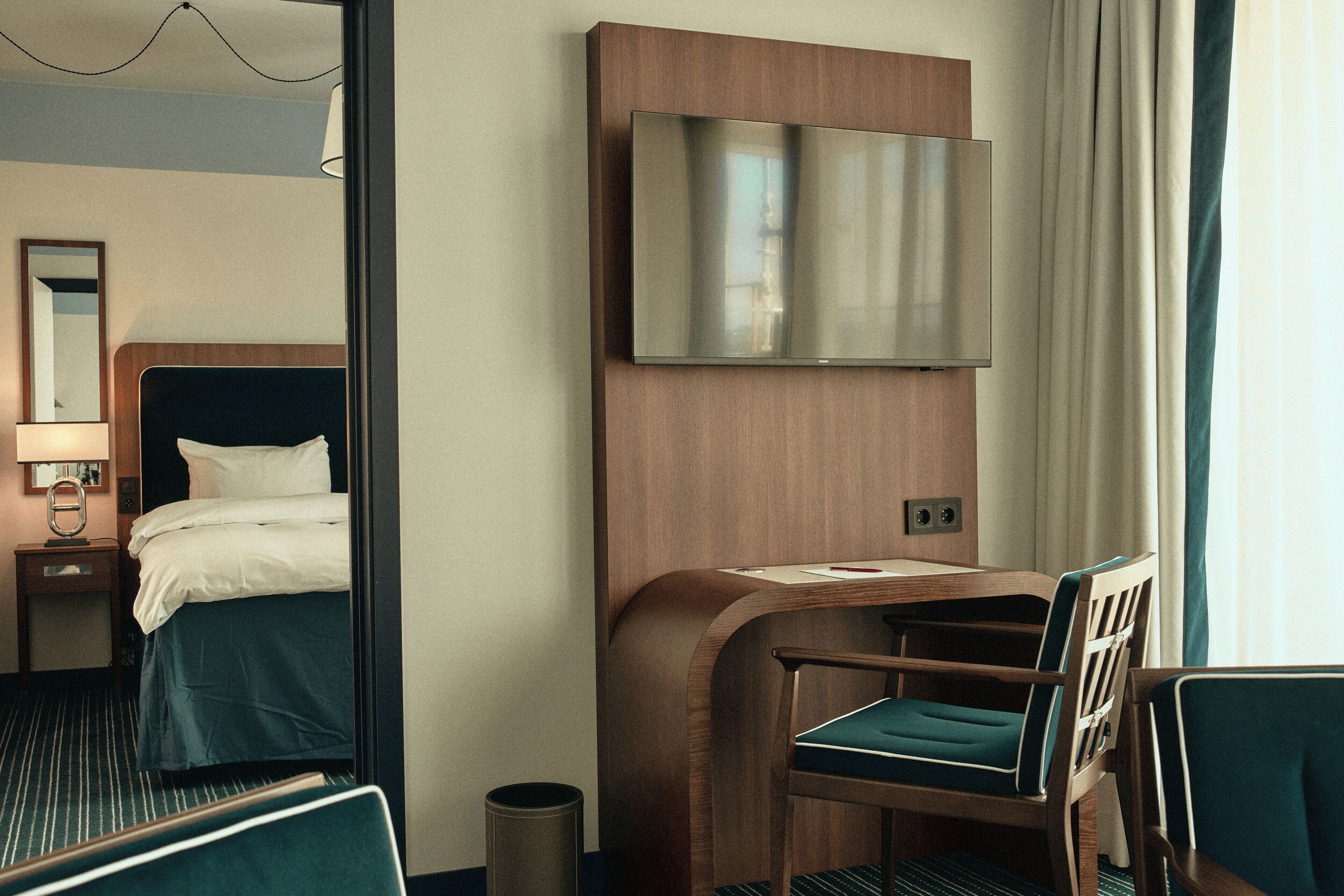 A hotel room with a bed, a desk with a chair, a television mounted on the wall, and a mirror on the wall.