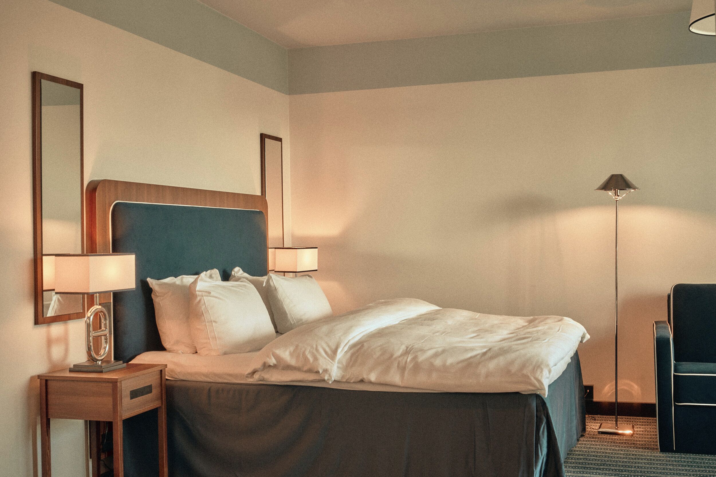 Een hotelkamer met een bed, nachtlampjes, een bureau, een stoel en een vloerlamp.