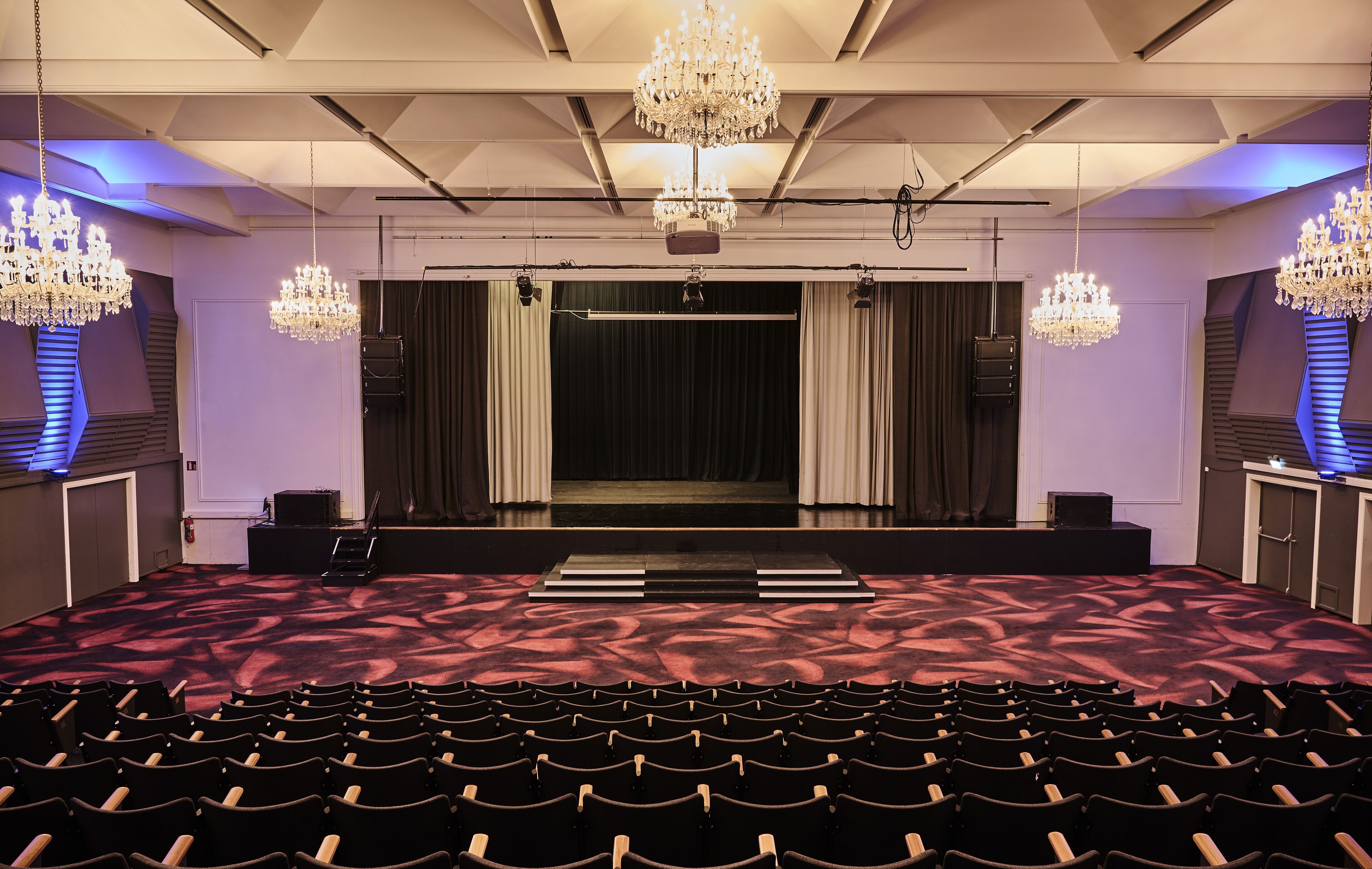 A theater with rows of seats, a stage with curtains, and chandeliers.
