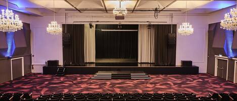 A theater with rows of seats, a stage with curtains, and chandeliers.