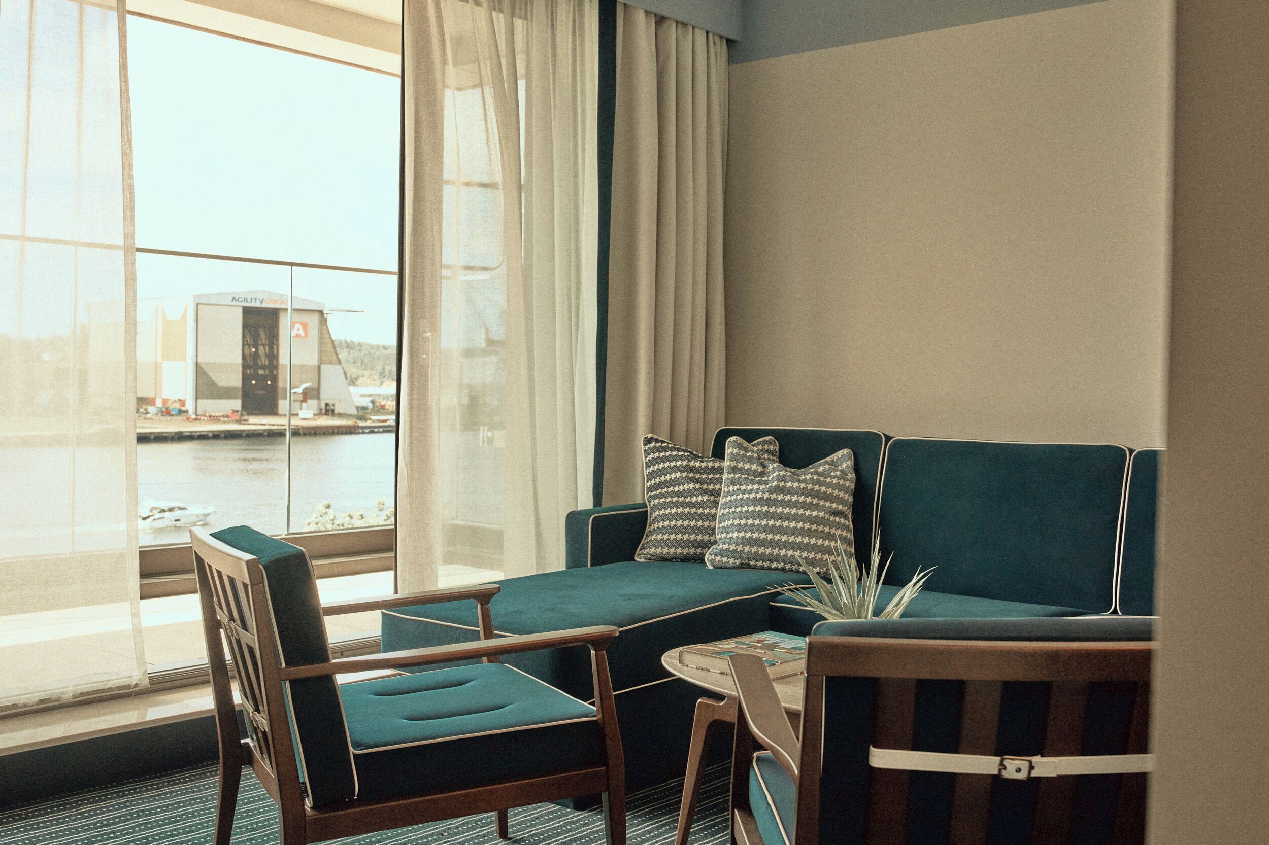 A hotel room with a view of a body of water, a green sofa, a wooden chair, and a small table.