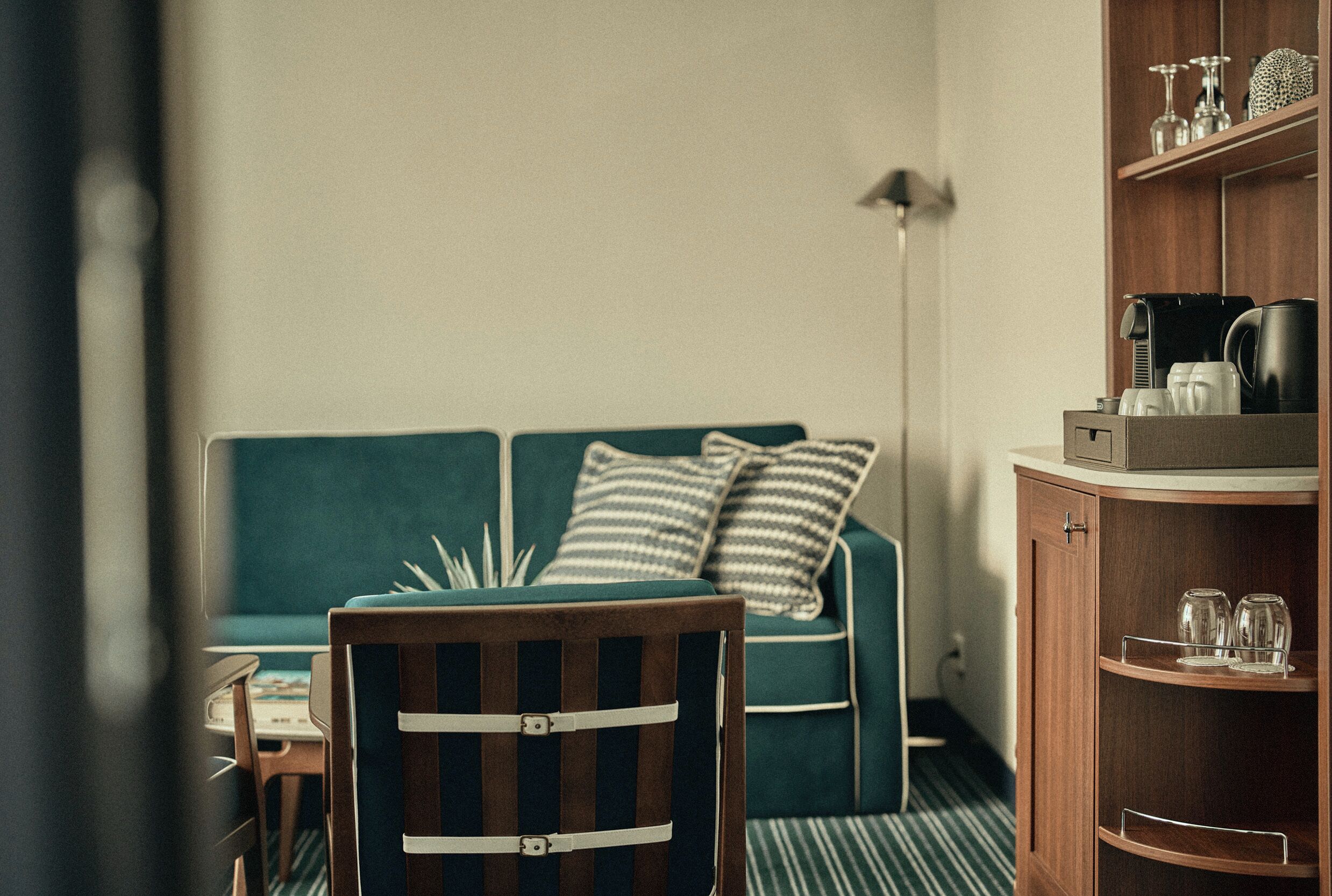 A room with a wooden chair, a green sofa with striped pillows, a small table, and a cabinet with glassware.