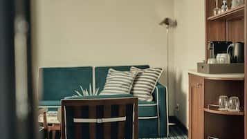 A room with a wooden chair, a green sofa with striped pillows, a small table, and a cabinet with glassware.