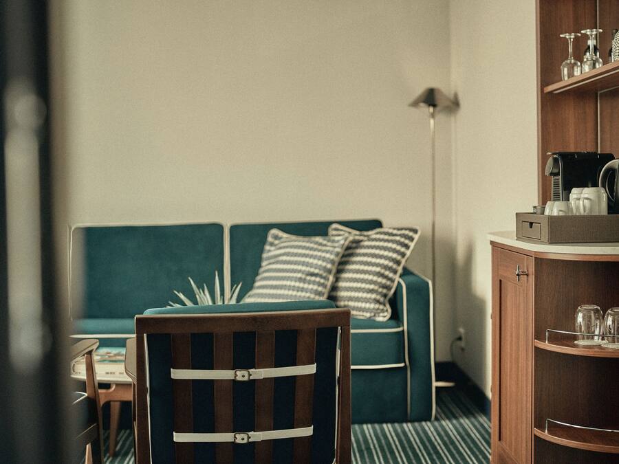 Une pièce comprenant une chaise en bois, un canapé vert avec des coussins à rayures, une petite table et un meuble contenant de la verrerie.