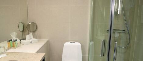A modern bathroom with a glass-enclosed shower, a white toilet, and a vanity with a mirror and toiletries.