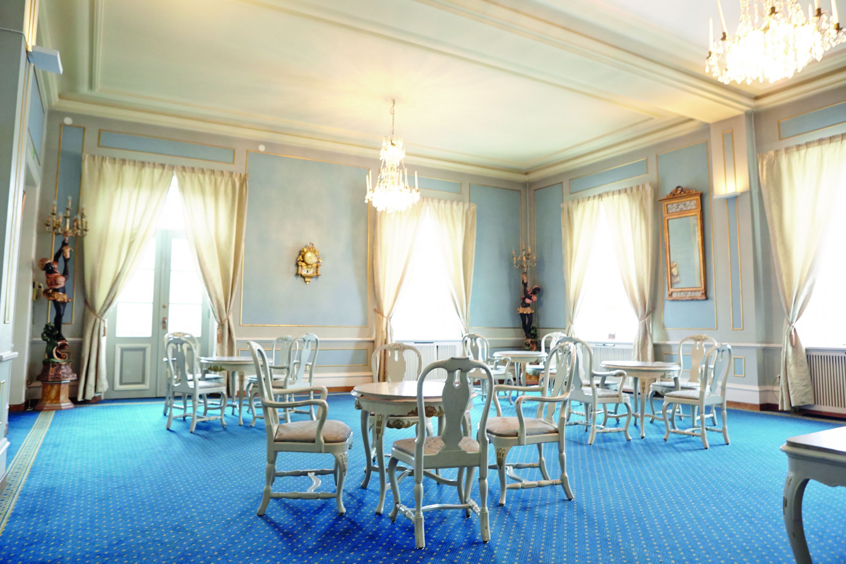 A room with blue carpet, white chairs, and a chandelier.