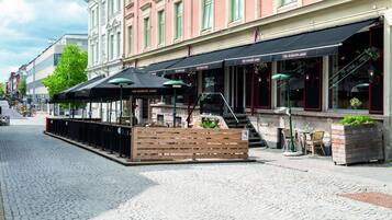 Rua de paralelepípedos com um restaurante chamado "The Bishop Arms", com mesas ao ar livre e uma cerca de madeira.