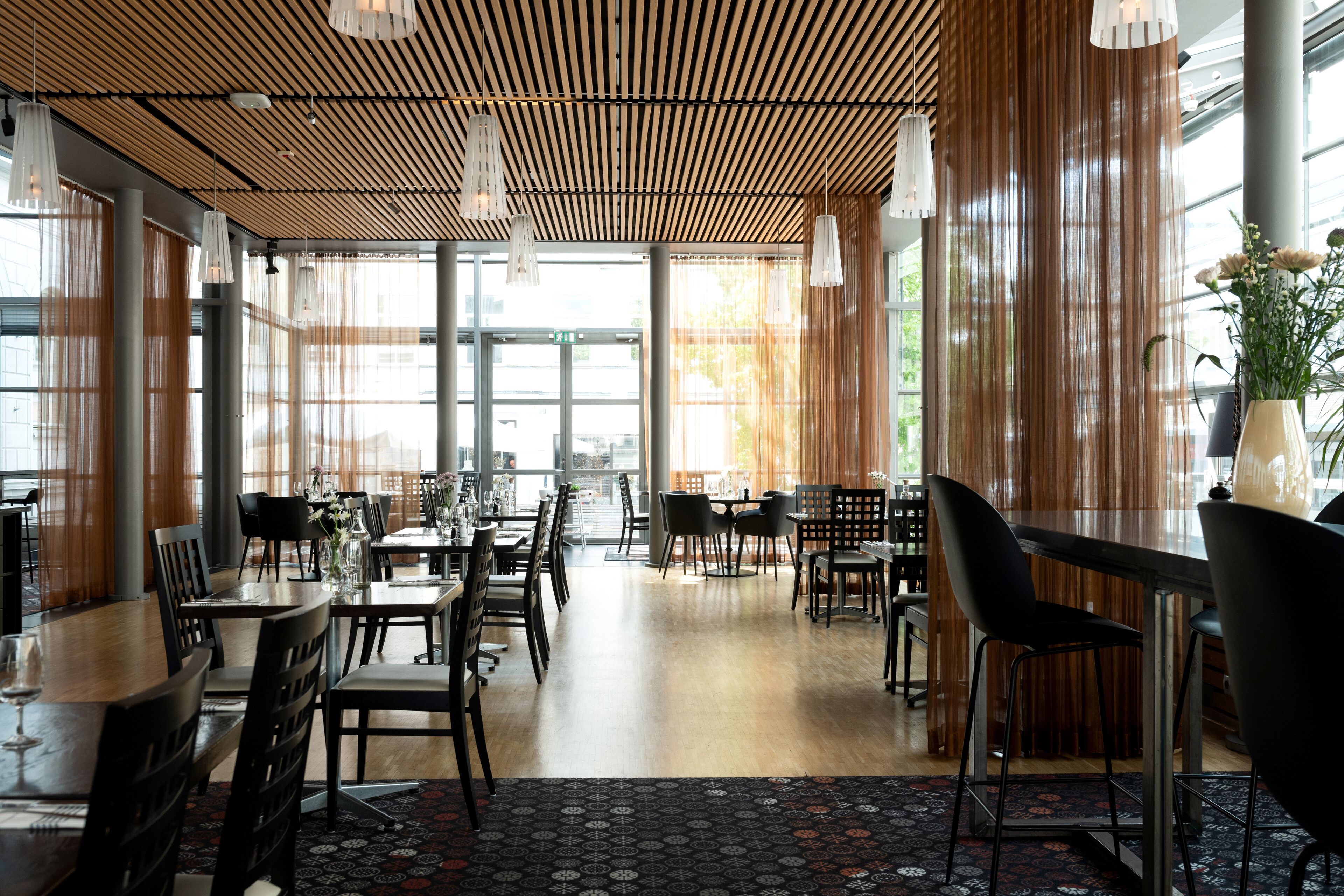 A spacious dining area with wooden flooring, modern chairs, and large windows allowing natural light.