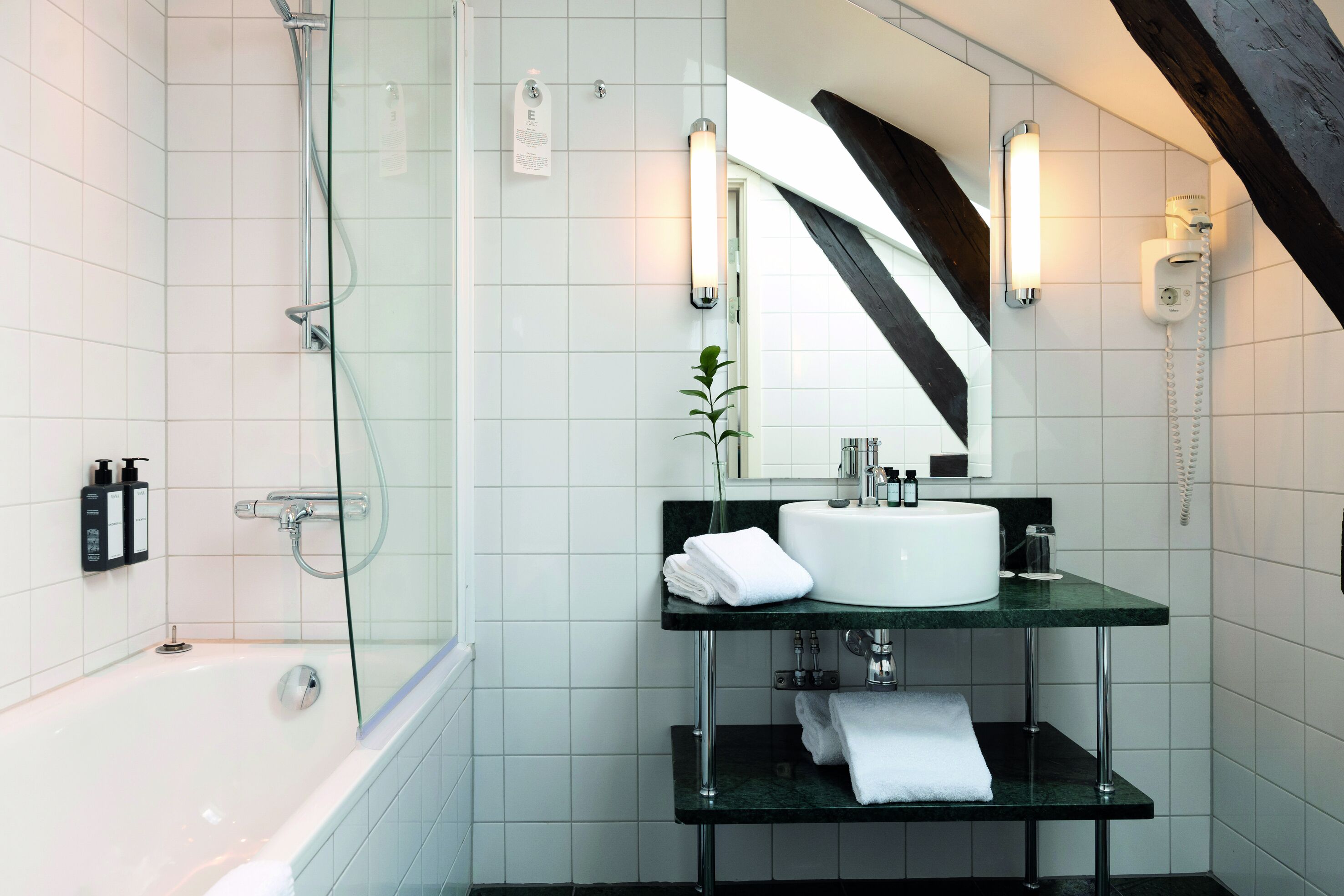 A modern bathroom with a glass shower enclosure, a white bathtub, a glass sink with a marble countertop, and a large mirror.