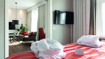 A hotel room with a bed, a TV, a desk with a chair, and a plant.