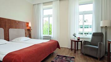 Une chambre d’hôtel avec un grand lit, une chaise, une petite table et une fenêtre avec des rideaux.