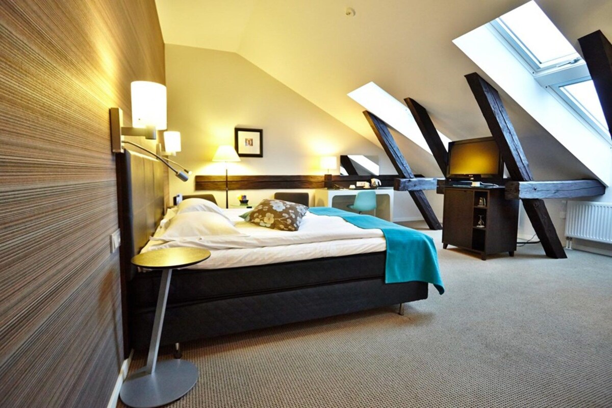 A modern hotel room with a bed, bedside tables, a desk, and a large skylight.