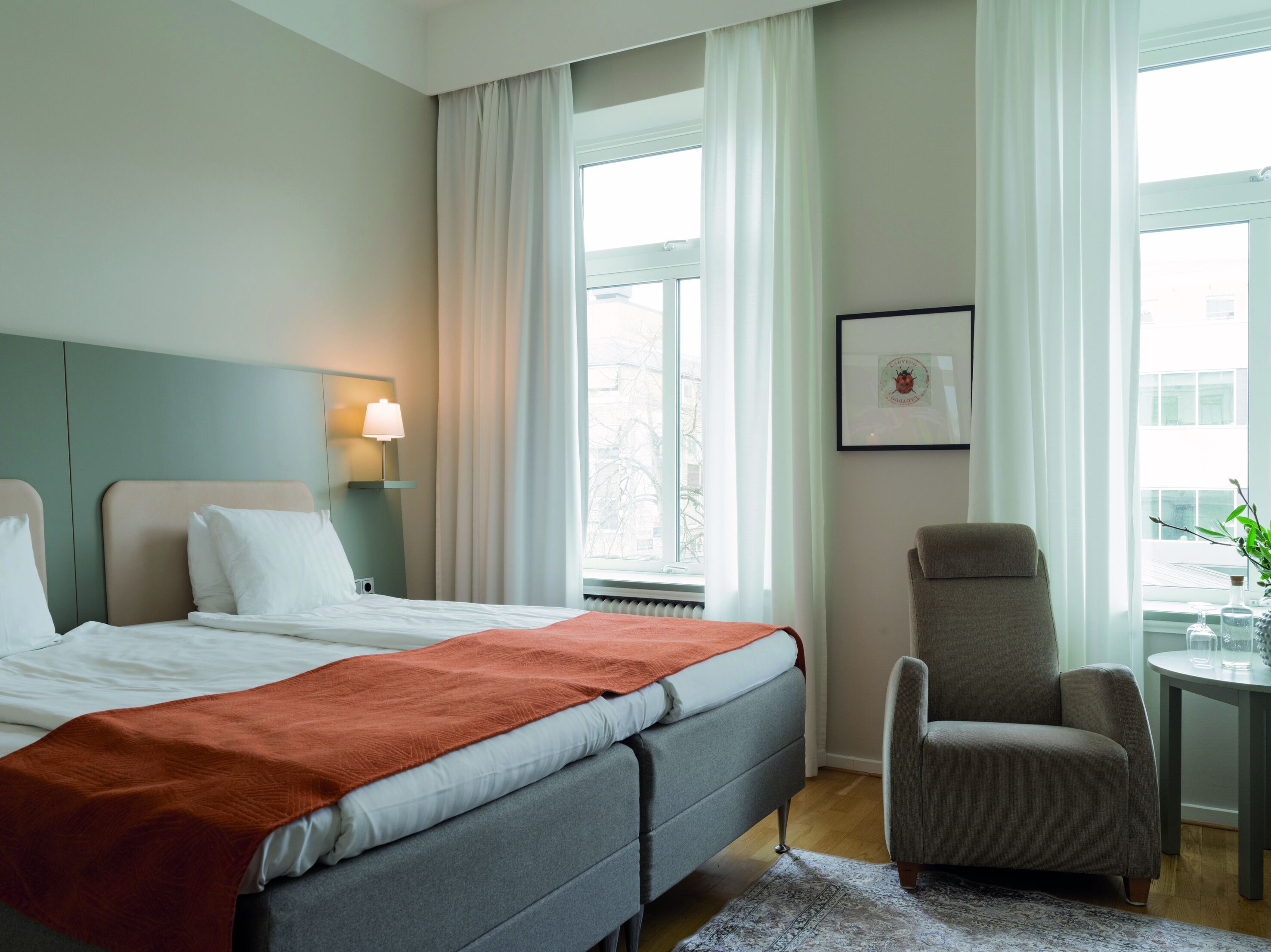 Ett hotellrum med två sängar, en stol, ett bord med glas och en inramad tavla på väggen.