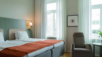 Ett hotellrum med två sängar, en stol, ett bord med glas och en inramad tavla på väggen.