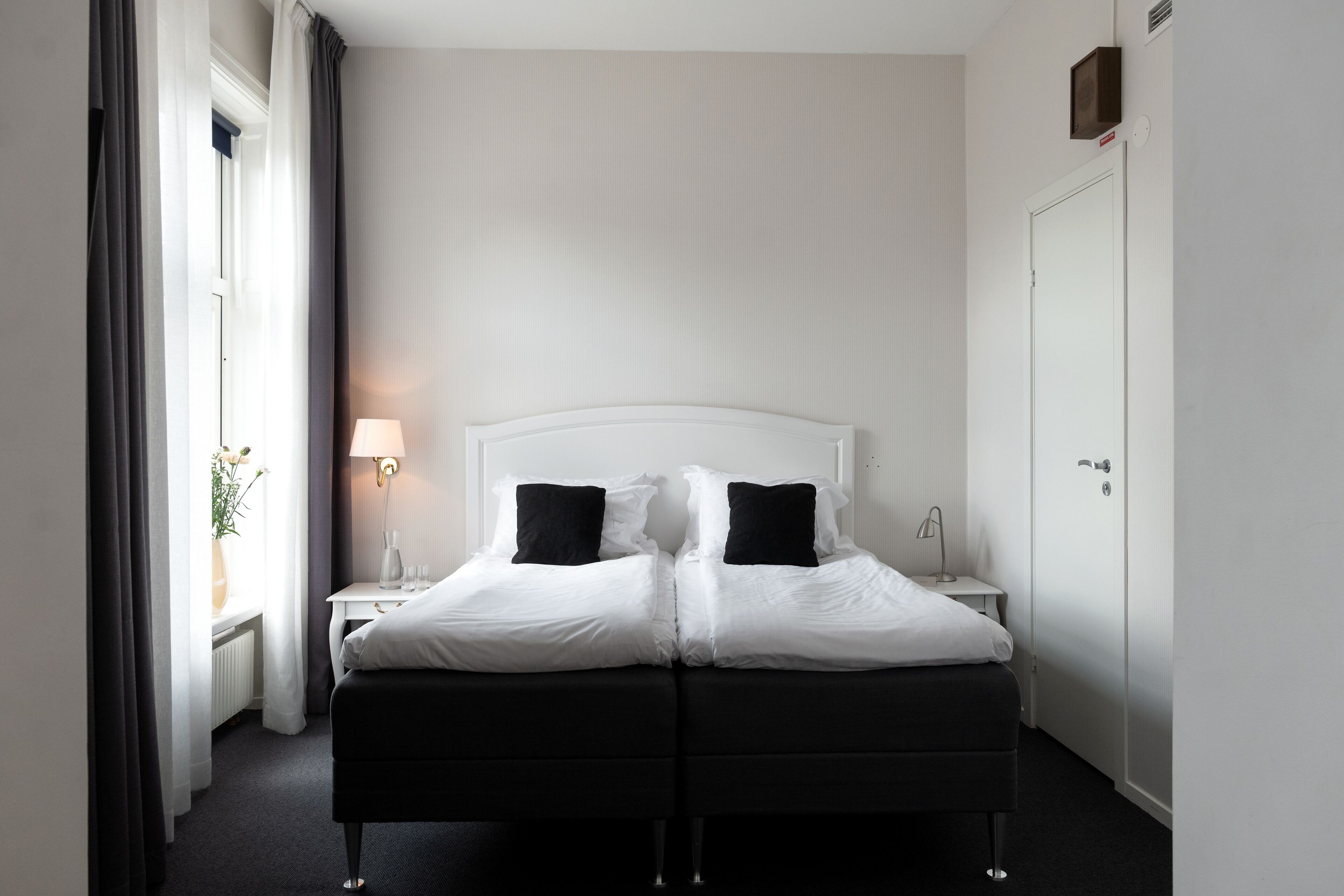 Una cama doble con ropa de cama blanco y negro, una mesita de noche con lámpara y un armario.