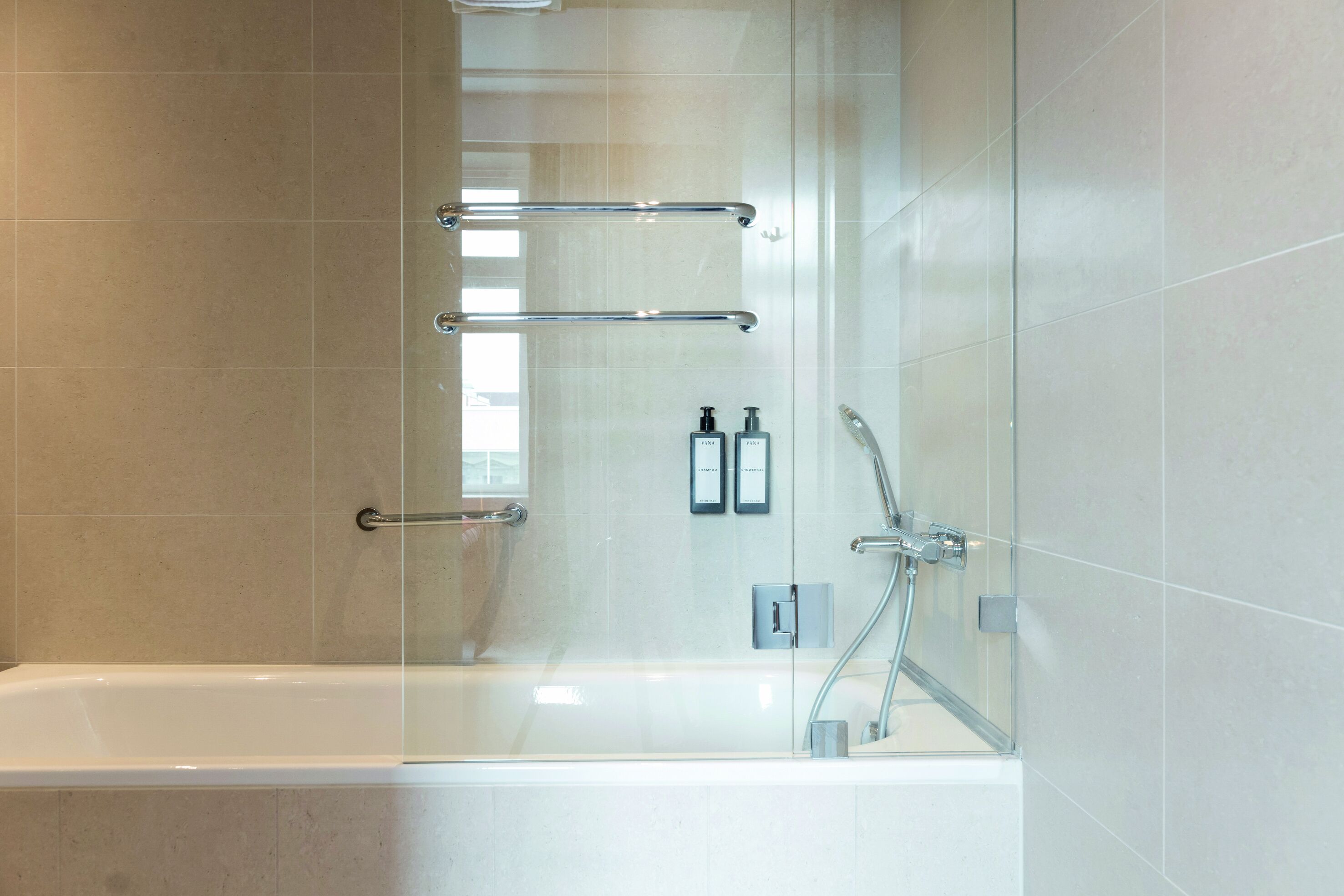 Ein modernes Badezimmer mit einer gläsernen Duschkabine, einer Badewanne und einer Handstange.