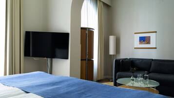 Una habitación de hotel con cama, televisor, sofá, una mesita con vasos y un cuadro enmarcado en la pared.