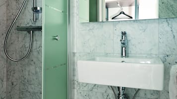 Un baño con ducha separada por vidrio, lavamanos blanco y pared con azulejos de mármol.