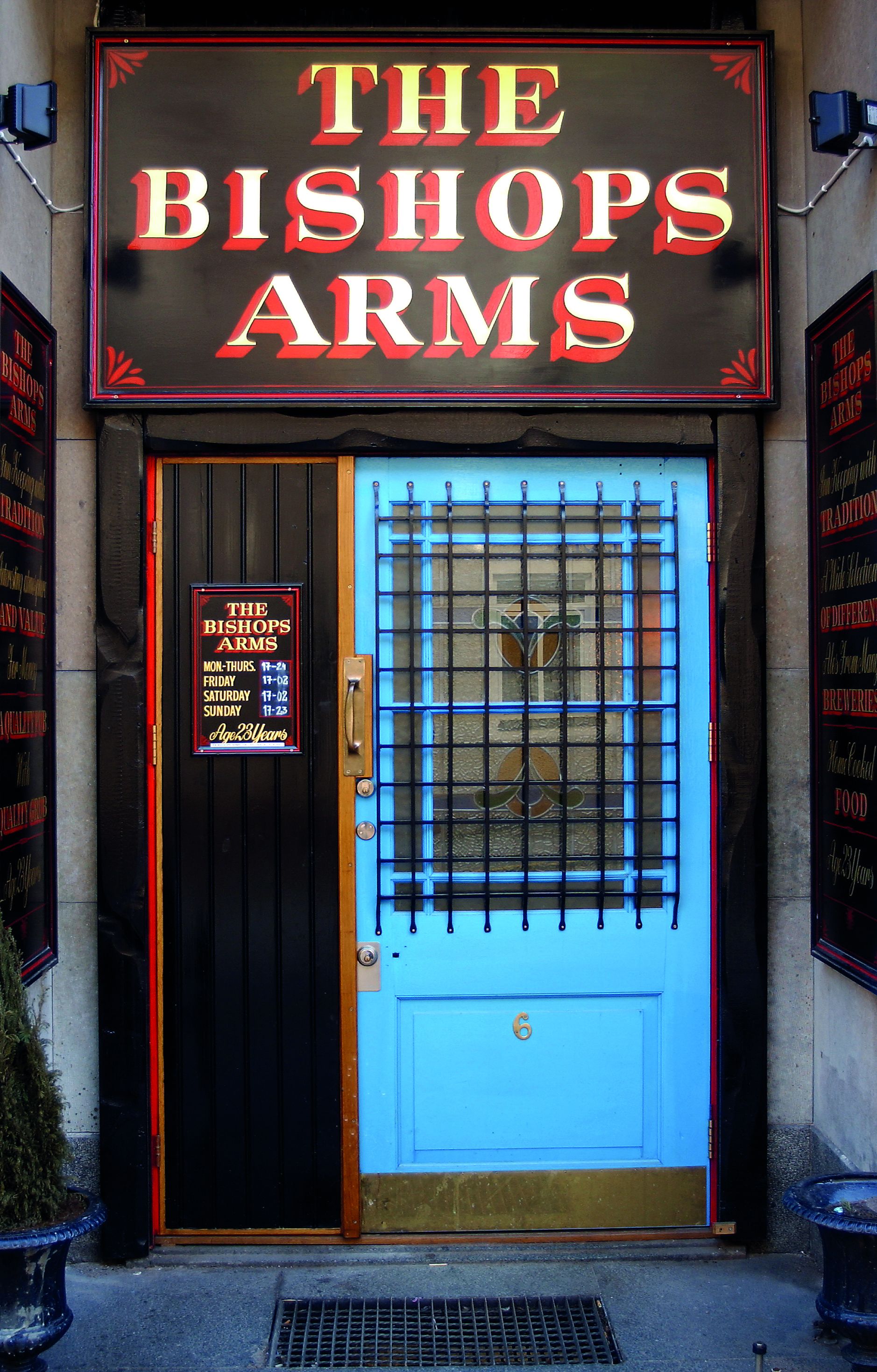 A building entrance with a sign reading "THE BISHOP'S ARMS" and a door with a blue panel and a number "6".