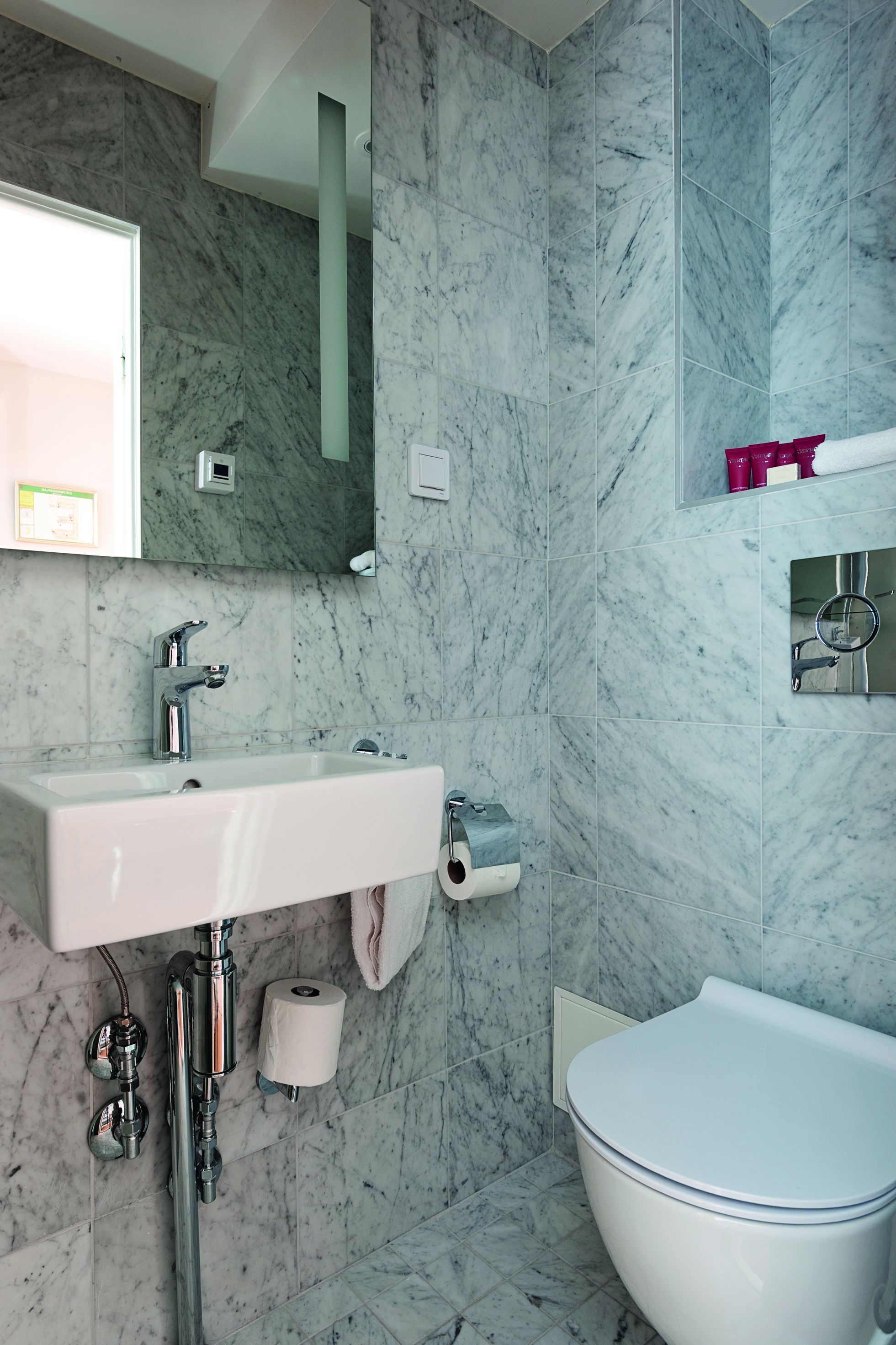 Un baño con lavamanos de mármol, inodoro y espejo.