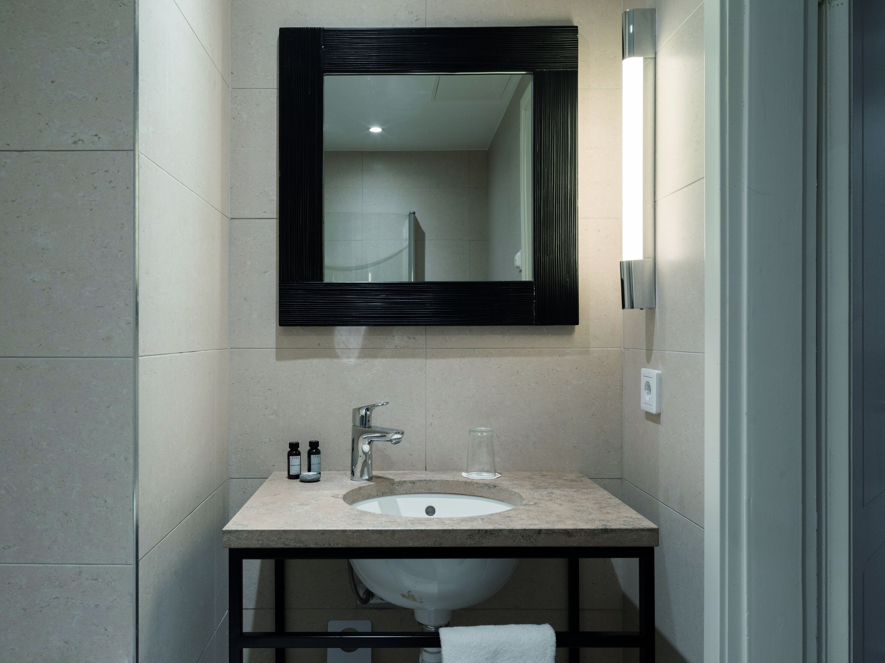A bathroom with a sink, mirror, and two bottles on the counter.